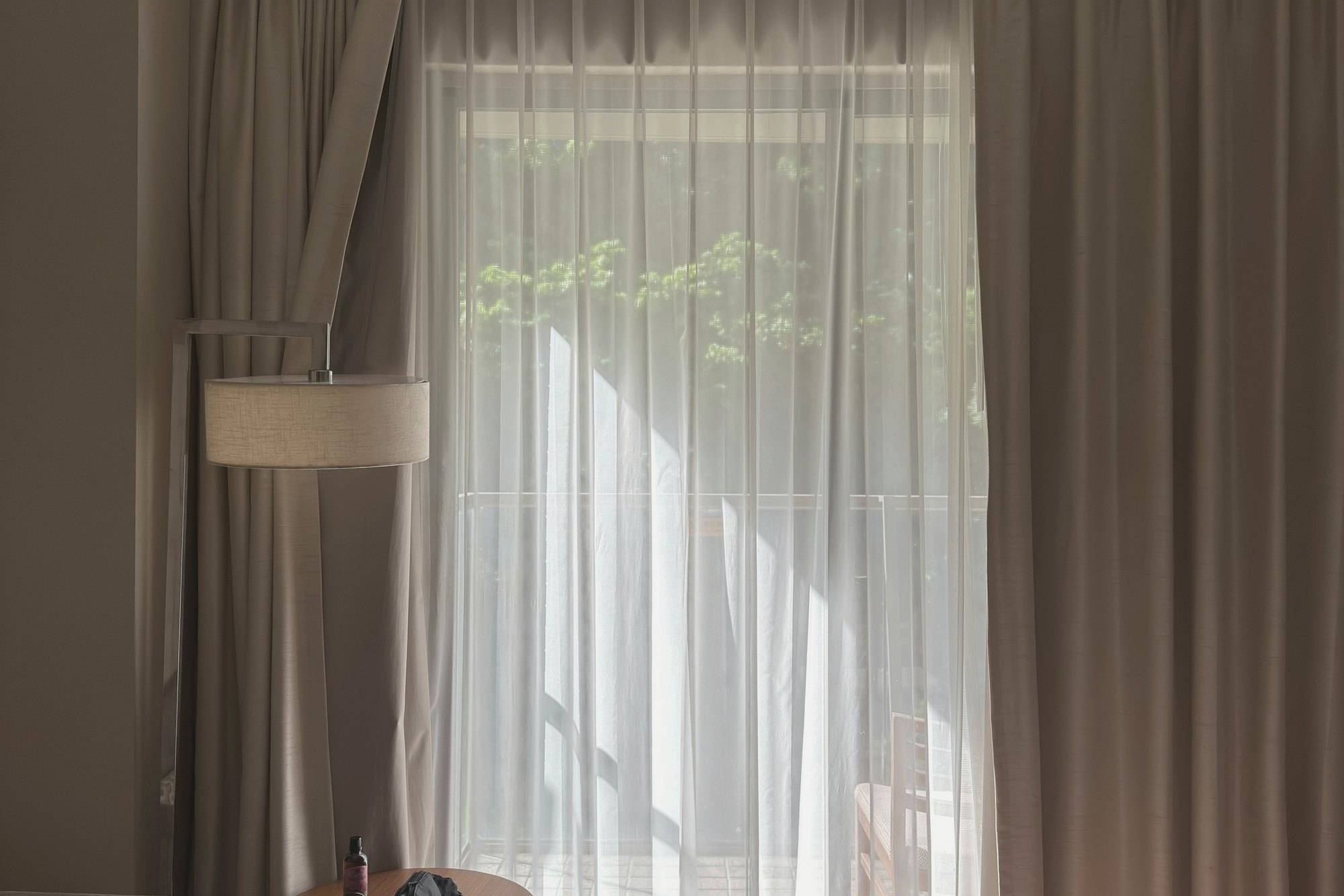 Sonnenlicht fällt durch helle Vorhänge in ein ruhiges Hotelzimmer mit Stehlampe