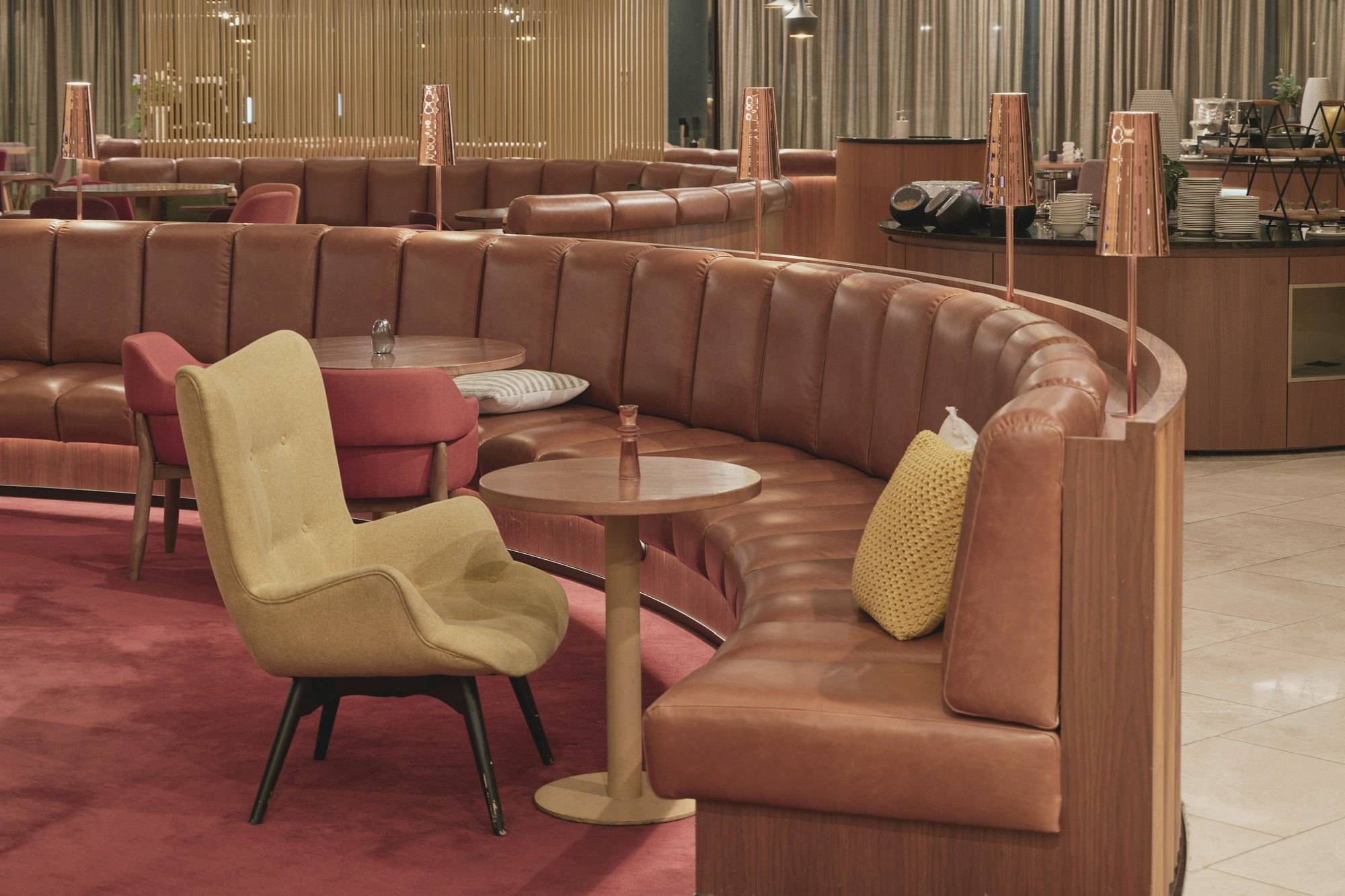 Halbrunde Lederbank, gelber Sessel und kleine Tische in einer ruhigen Lounge mit warmem Licht